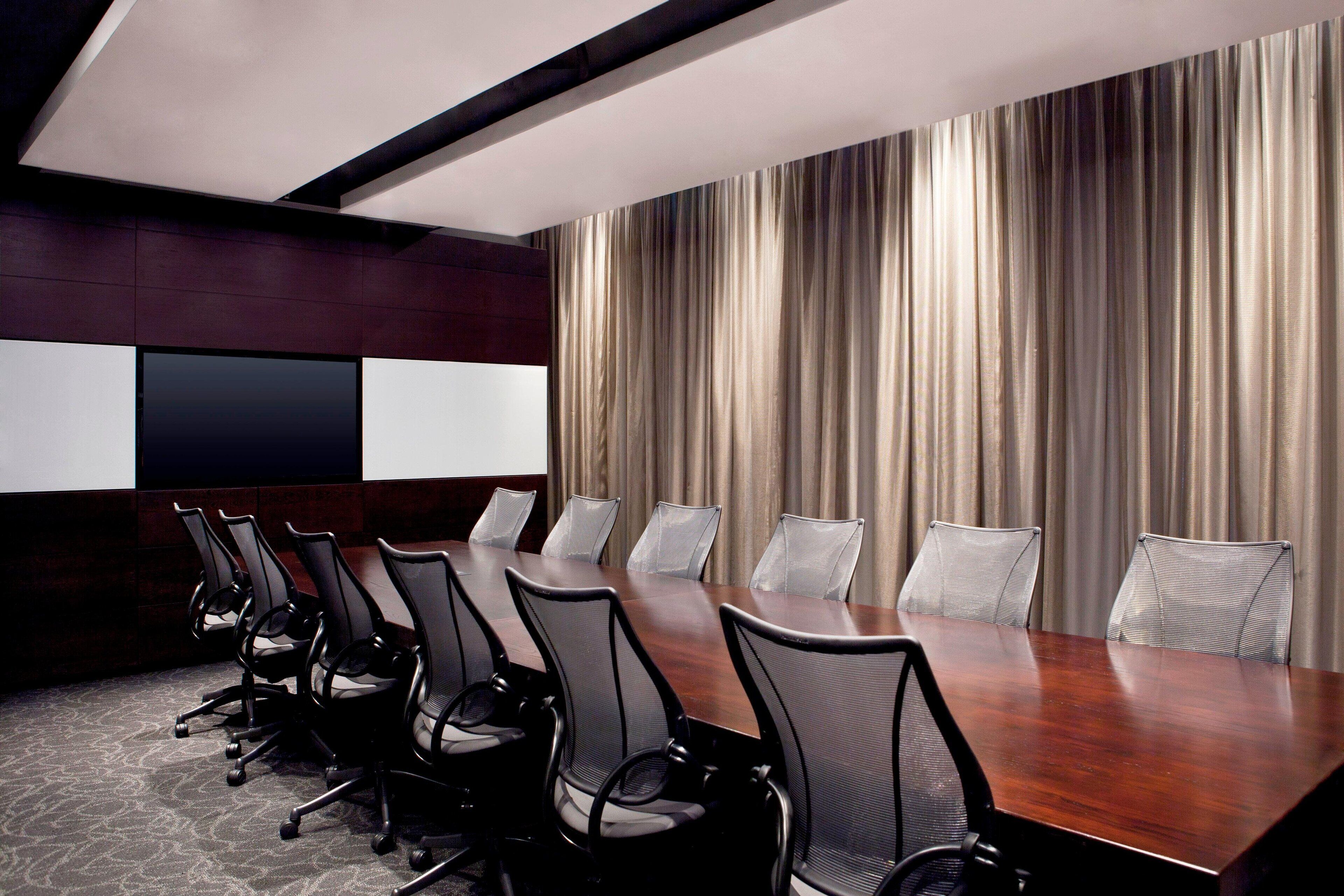 A conference room with a long table, black mesh chairs, and a large curtain backdrop.