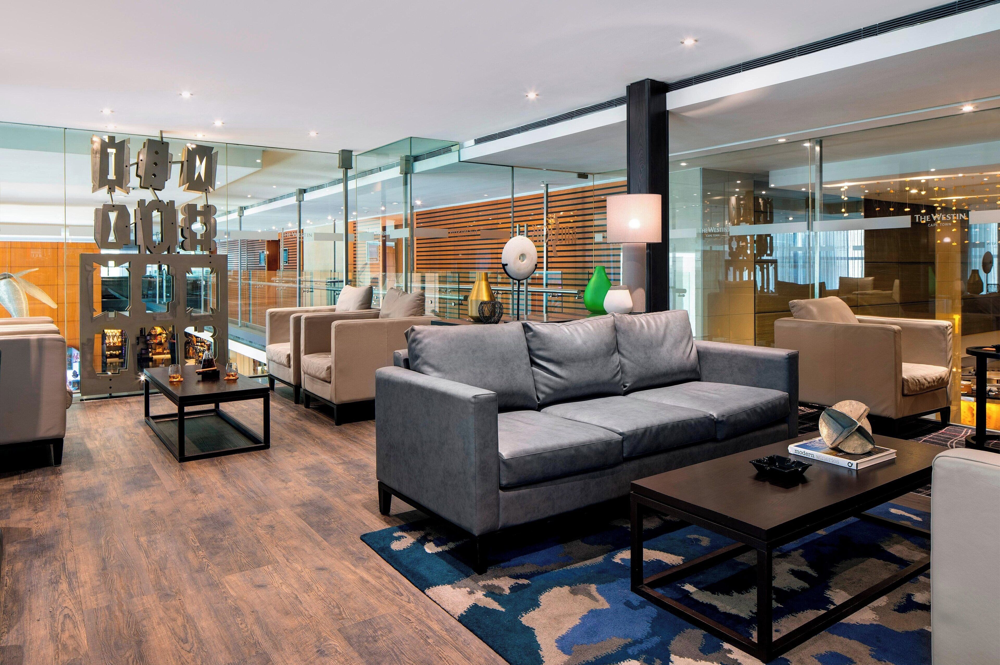 A modern hotel lobby with a grey sofa, a coffee table, and a glass partition with a decorative metal frame.