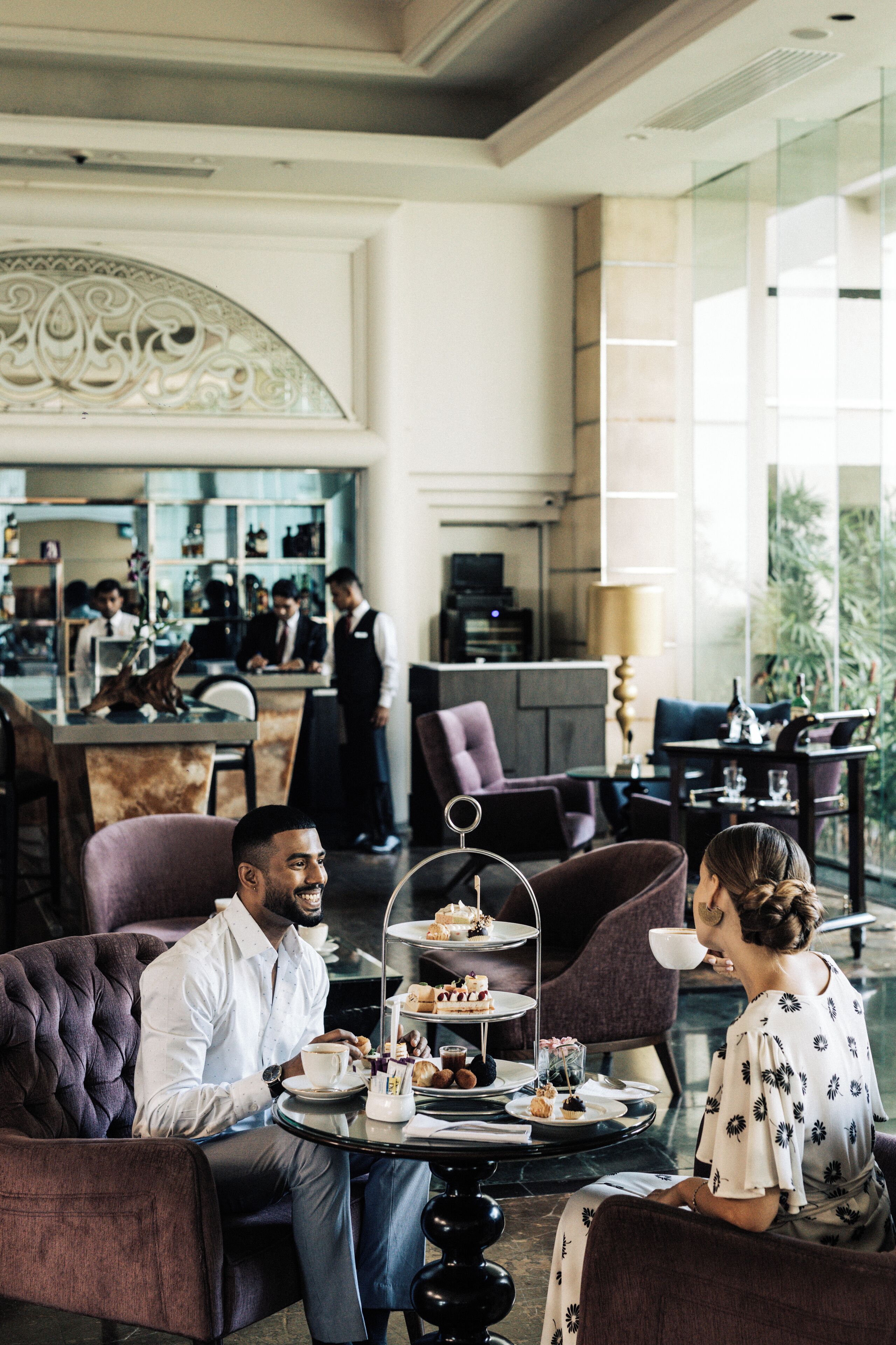 Un moderno hall de hotel con un carrito de postres de tres niveles, asientos cómodos y una zona de bar al fondo.