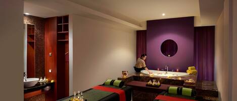 A modern spa room with a large bathtub, a massage table, and a small seating area.