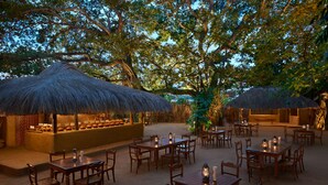 An outdoor dining area with wooden tables and chairs, thatched umbrellas, and lanterns.
