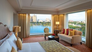 A hotel room with a large bed, a sofa, a chair, a small table, and a view of a cityscape and water.
