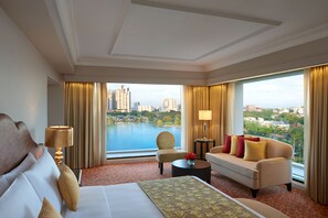 A hotel room with a large bed, a sofa, a chair, a small table, and a view of a cityscape and water.