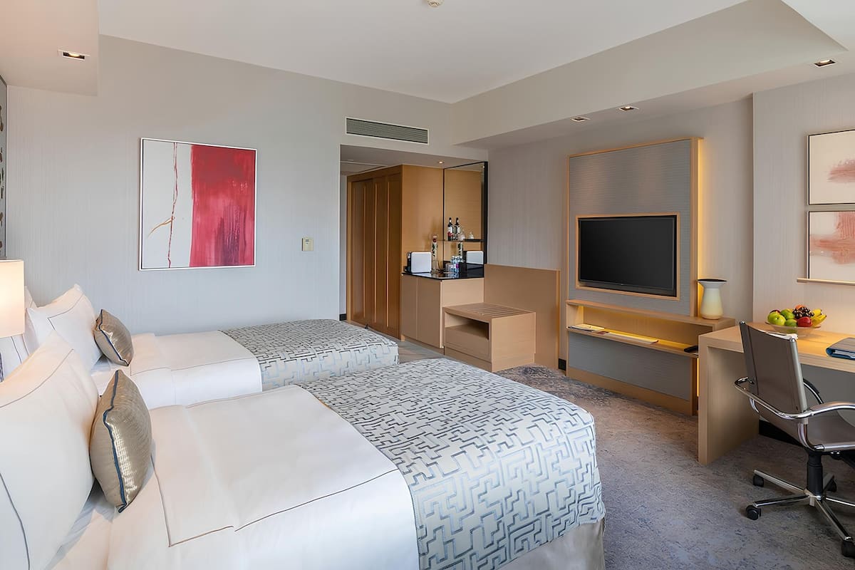 Ett hotellrum med två sängar, ett skrivbord, en TV och ett litet pentry.