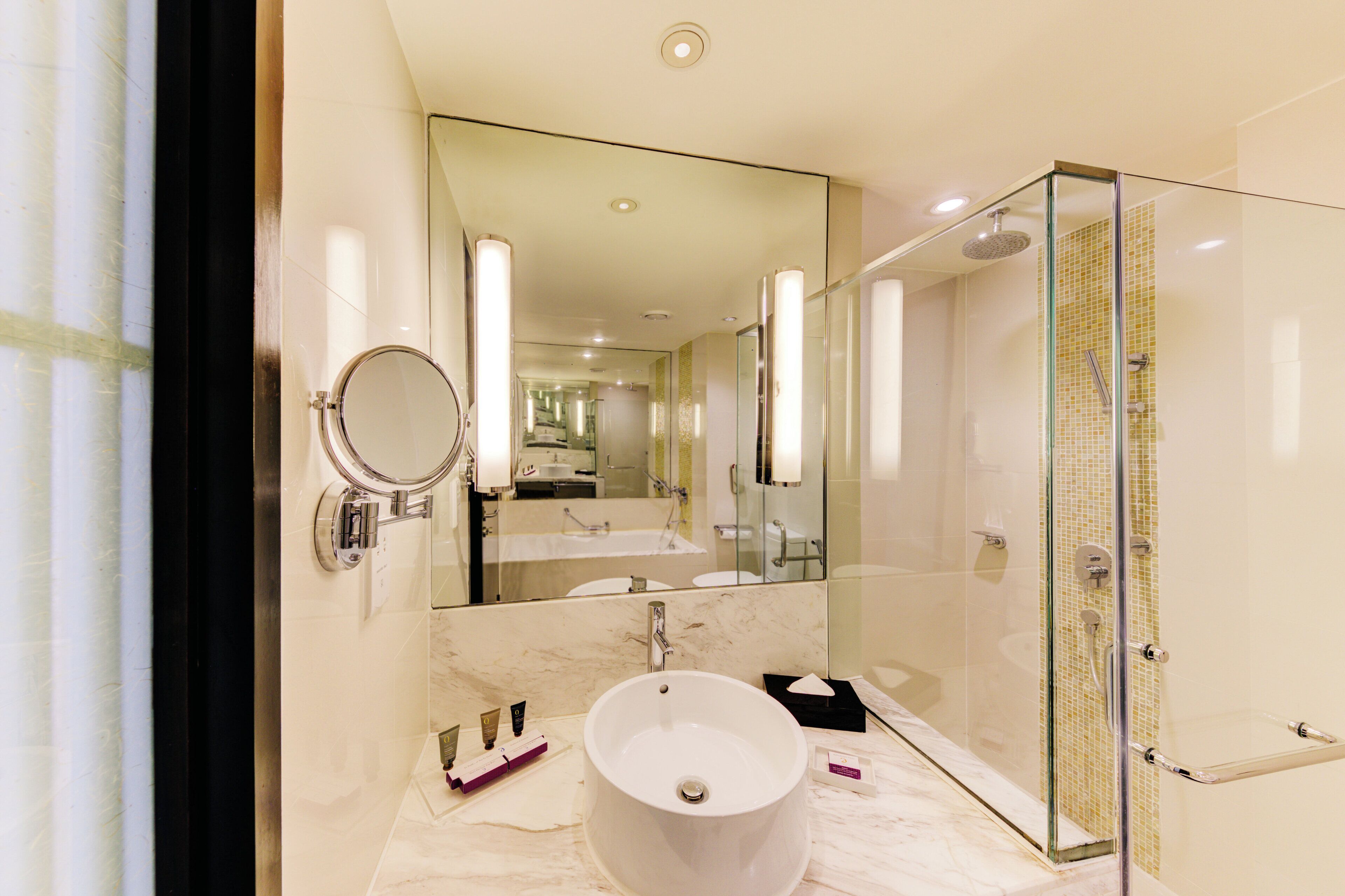 A modern bathroom with a large mirror, a round sink, and a glass-enclosed shower.