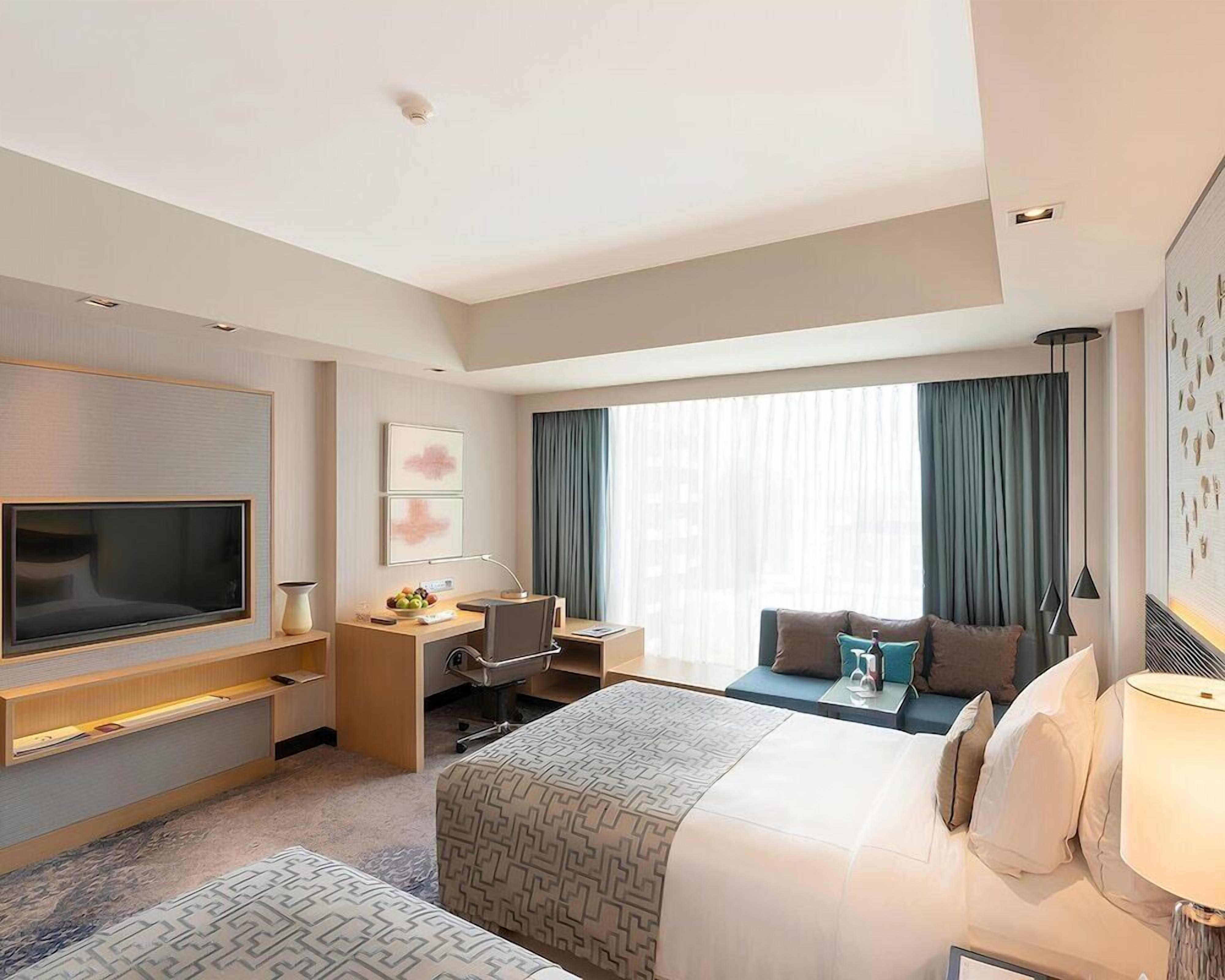A hotel room with a bed, a desk, a TV, a chair, and a sofa.