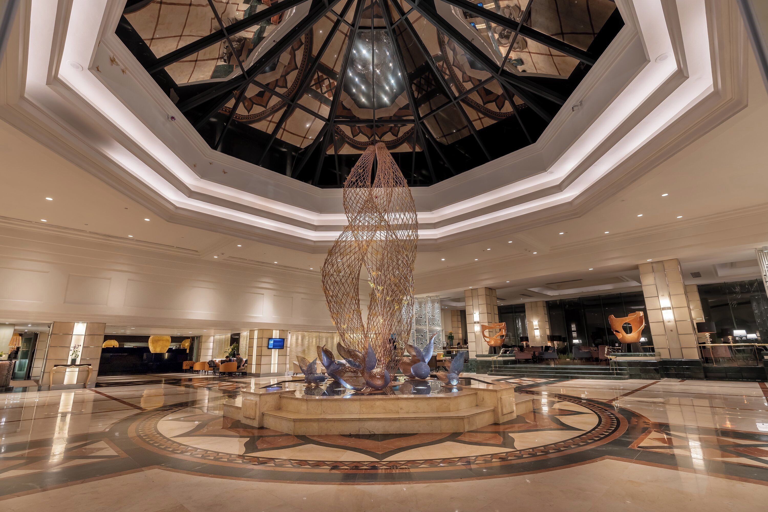 Un hall d’entrée spacieux agrémenté d’une œuvre d’art centrale, un plafond haut orné d’un motif géométrique et un sol poli.