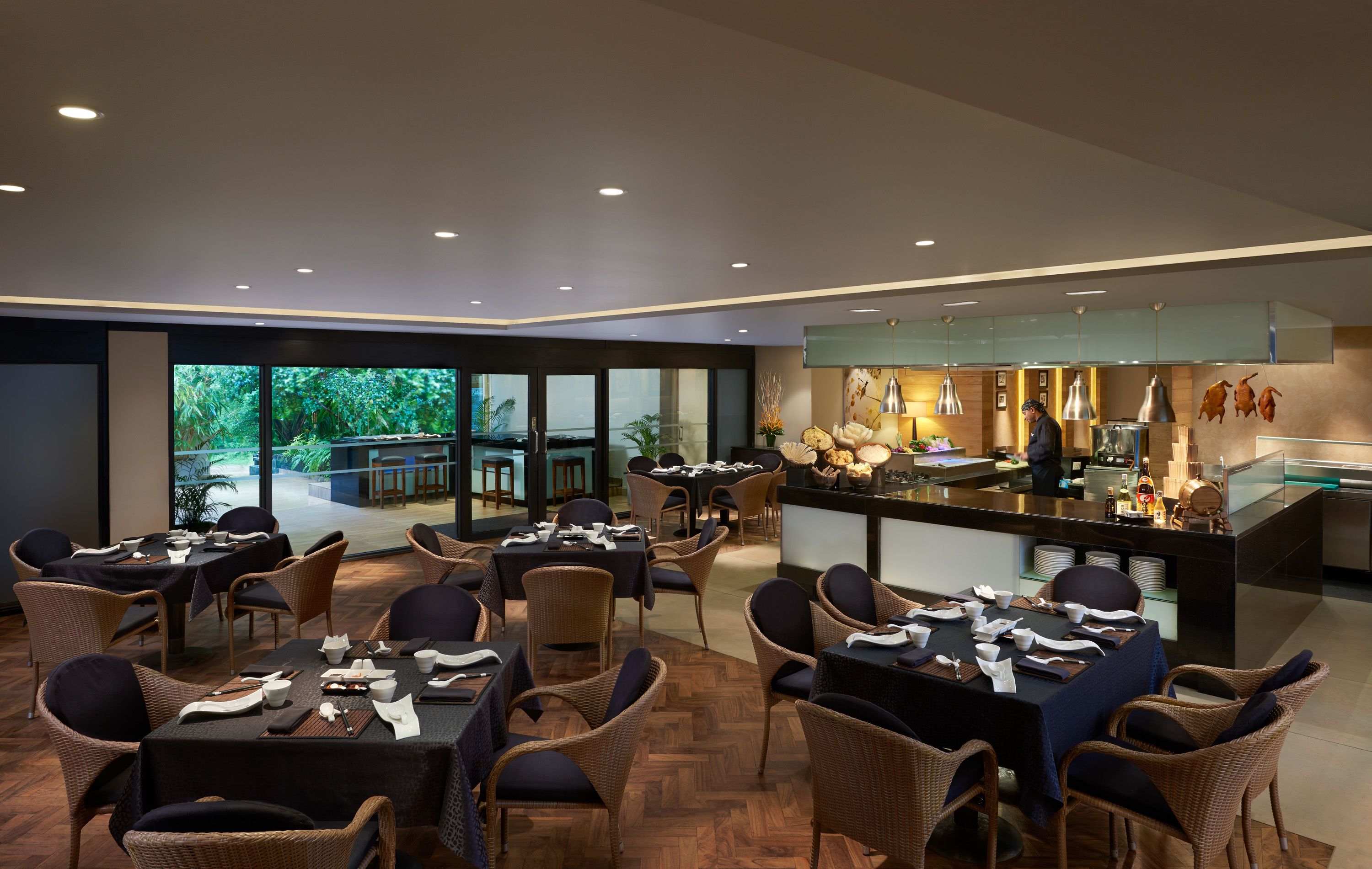 A modern dining area with tables set for service, a bar area, and large windows offering a view of the outdoors.