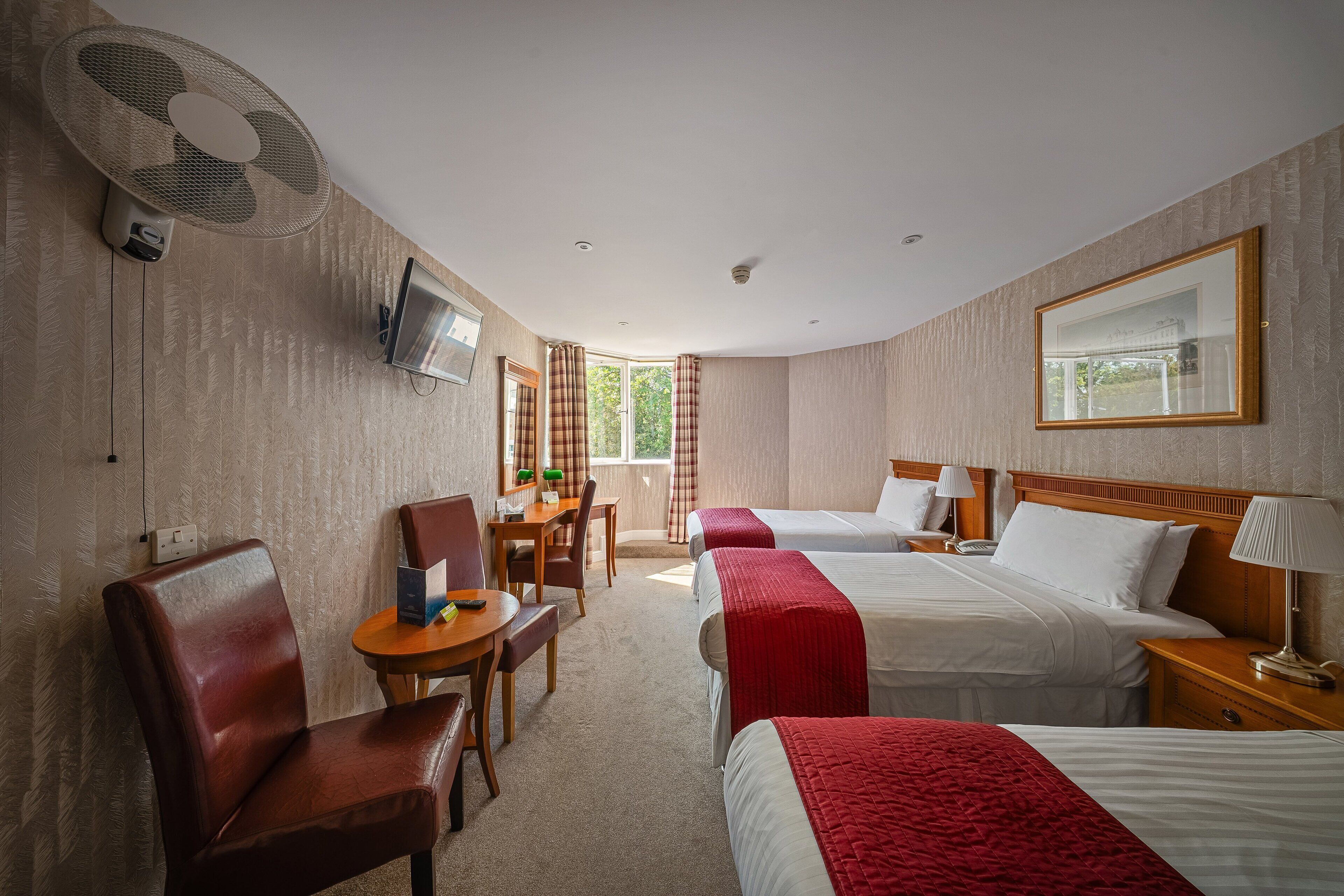 Quarto de hotel com duas camas, uma escrivaninha, uma cadeira, uma televisão e uma janela com cortinas.