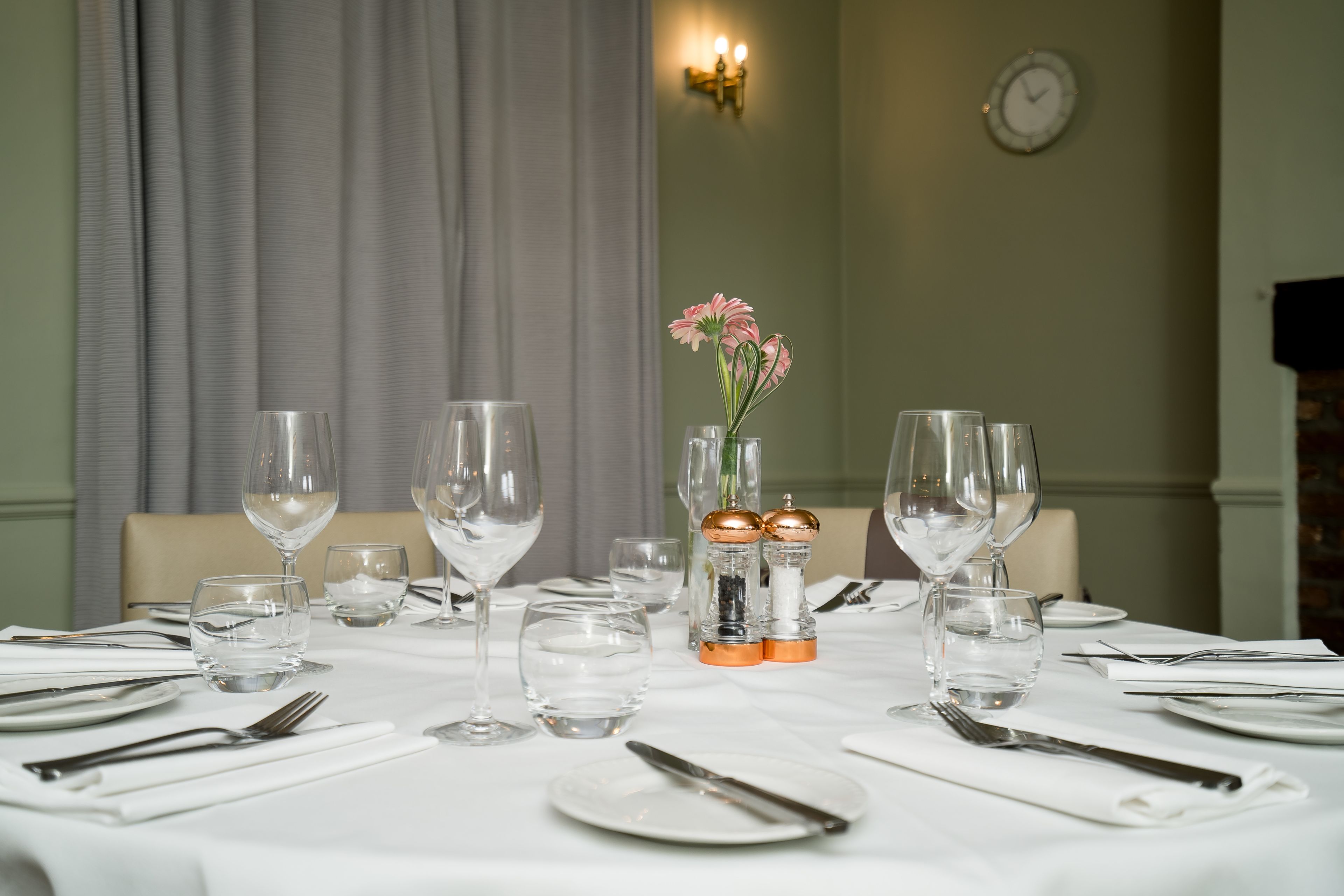 Mesa de comedor puesta con mantel blanco, platos, cubiertos y vasos de agua.