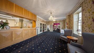 A hotel lobby with a reception desk, seating area, and floral wallpaper.