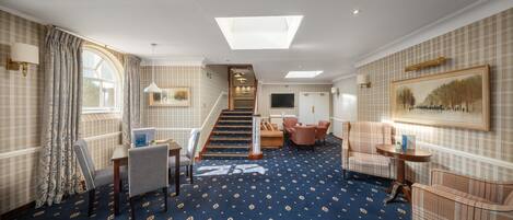 A hotel lobby with a patterned carpet, a staircase, seating area, and a television mounted on the wall.