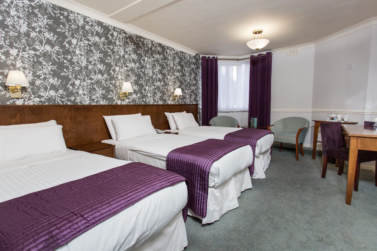 Een hotelkamer met drie bedden, een houten hoofdeinde, een eettafel en een stoel.