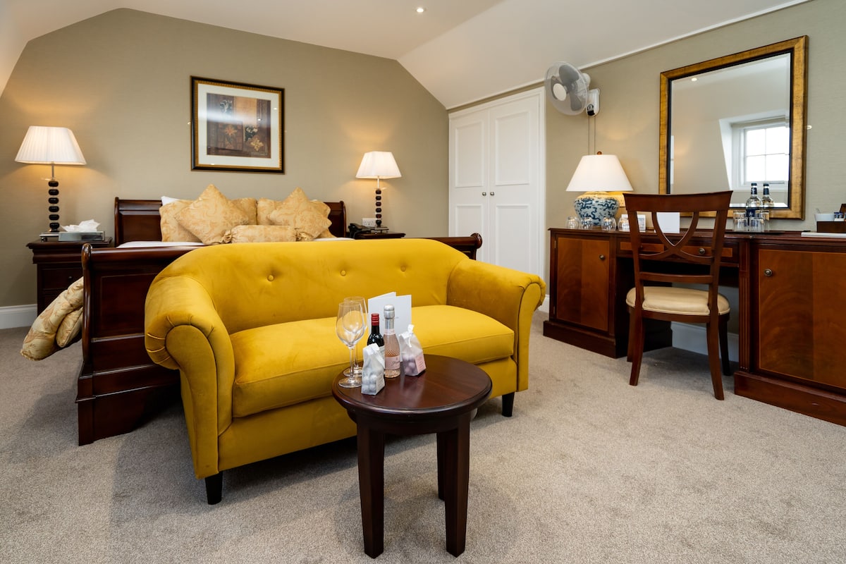Een hotelkamer met een gele bank, een houten dressoir, een spiegel en twee lampen.