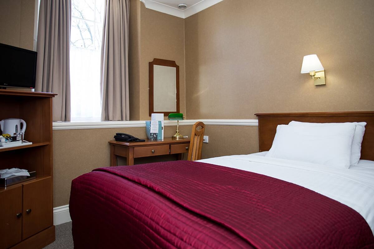 Een hotelkamer met een bed, een bureau, een televisie, een lamp en een raam met gordijnen.