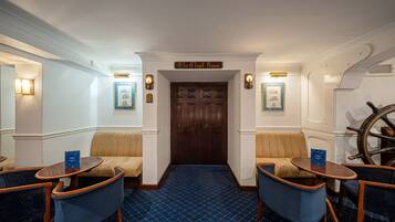 Una habitación con una puerta de madera con la leyenda "The Chart Room", alfombra azul estampada y dos sillones azules con estructura de madera.