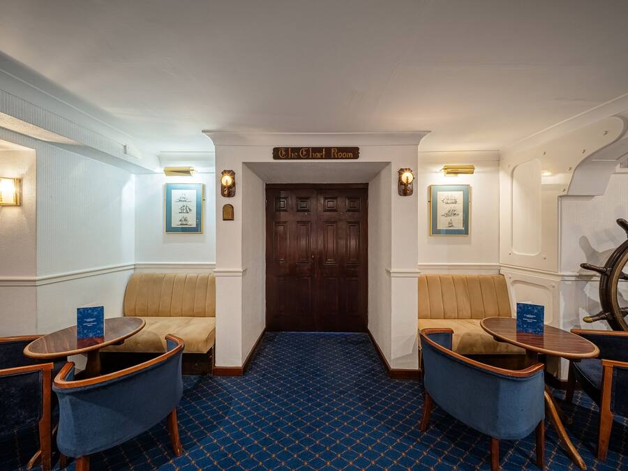 Una habitación con una puerta de madera con la leyenda "The Chart Room", alfombra azul estampada y dos sillones azules con estructura de madera.