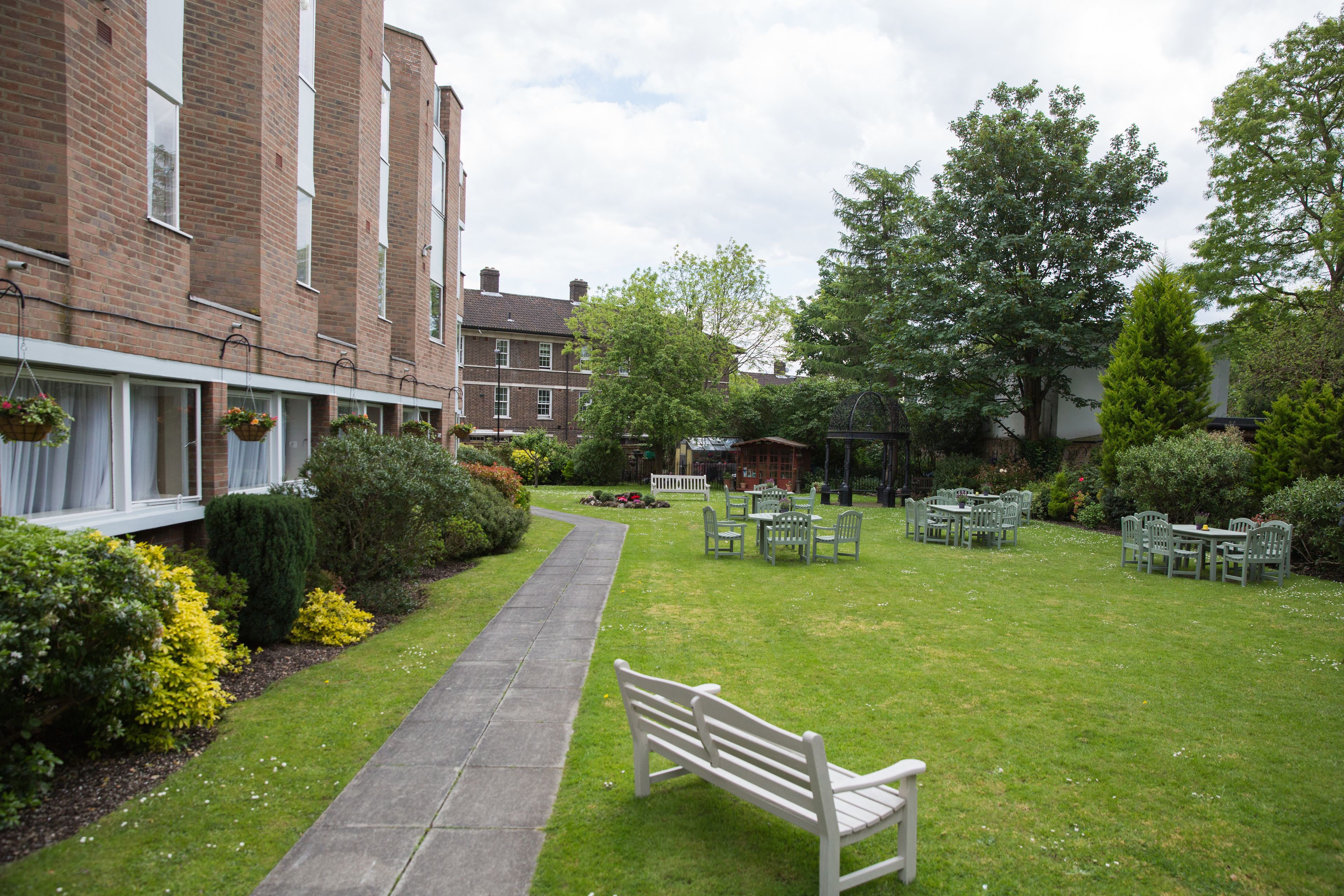 A courtyard with a bench, outdoor seating, and a pathway leading to a building with hanging flower baskets.