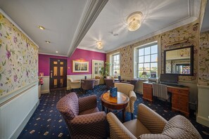 Un vestíbulo de hotel con papel tapiz estampado, una pared de acento morada y un área de estar con sofás y sillones estampados.