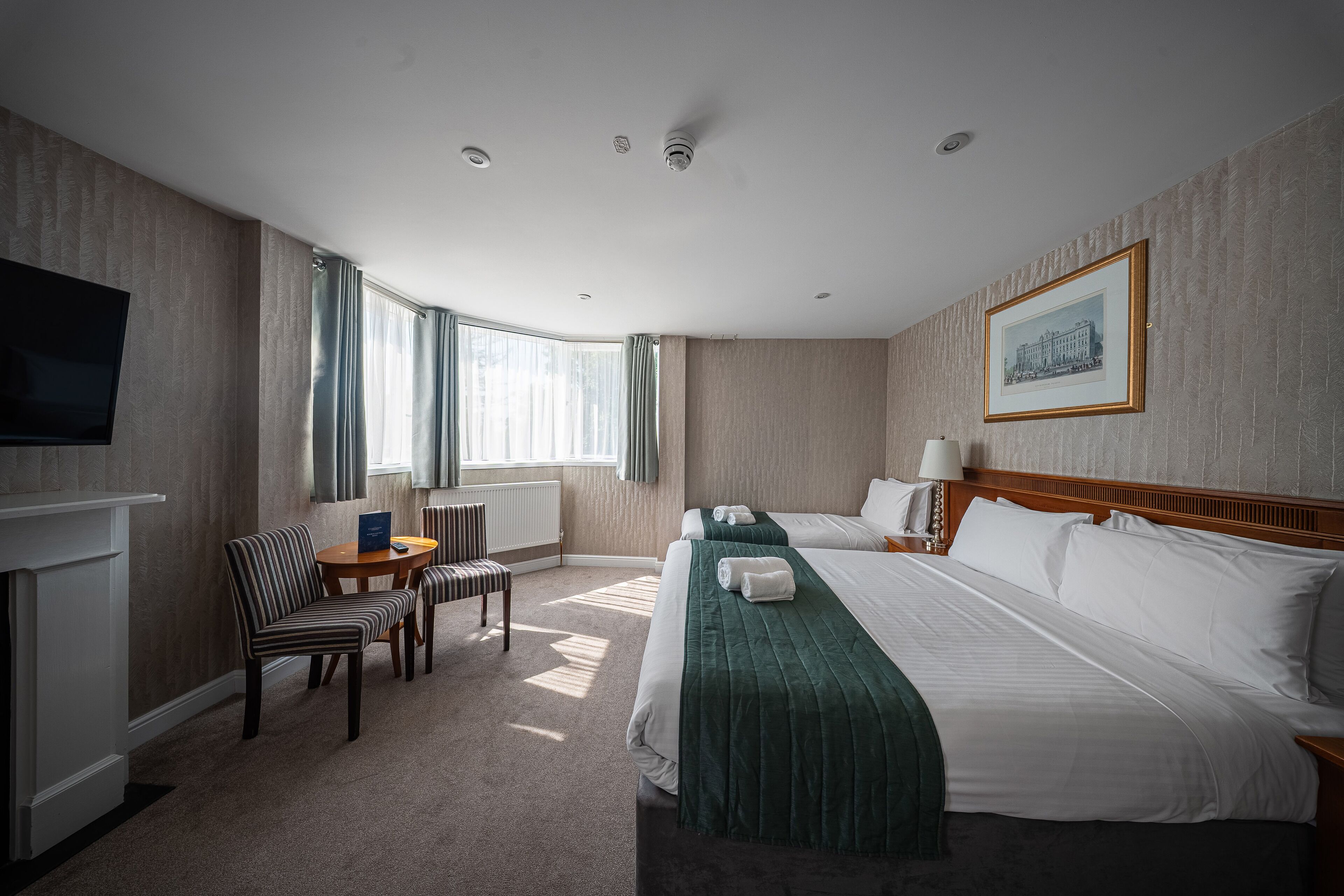A hotel room with a large bed, a smaller bed, a TV, a desk with a chair, and a window with curtains.