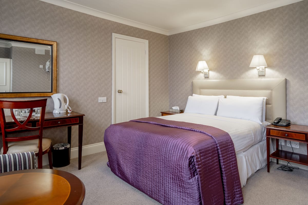 Een hotelkamer met een bed, een bureau met stoel, een telefoon en een spiegel.