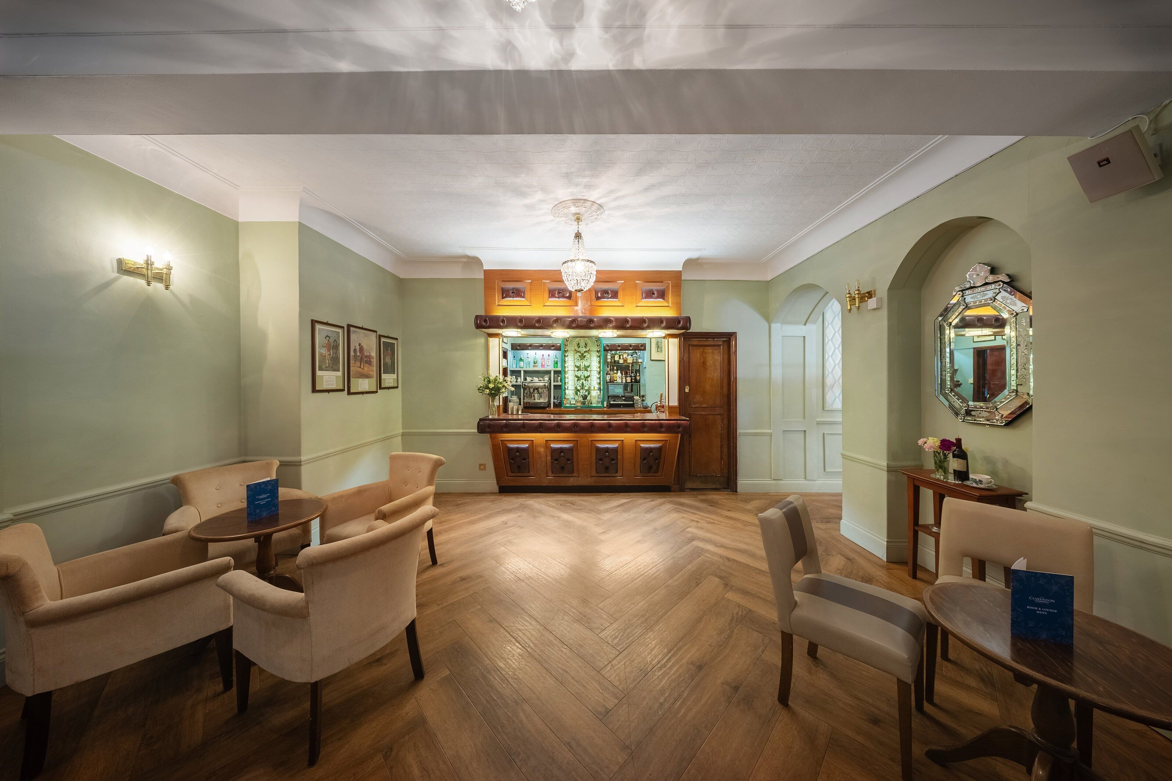 A spacious room with a wooden herringbone floor, a bar area with a mirror and framed pictures, and a chandelier.