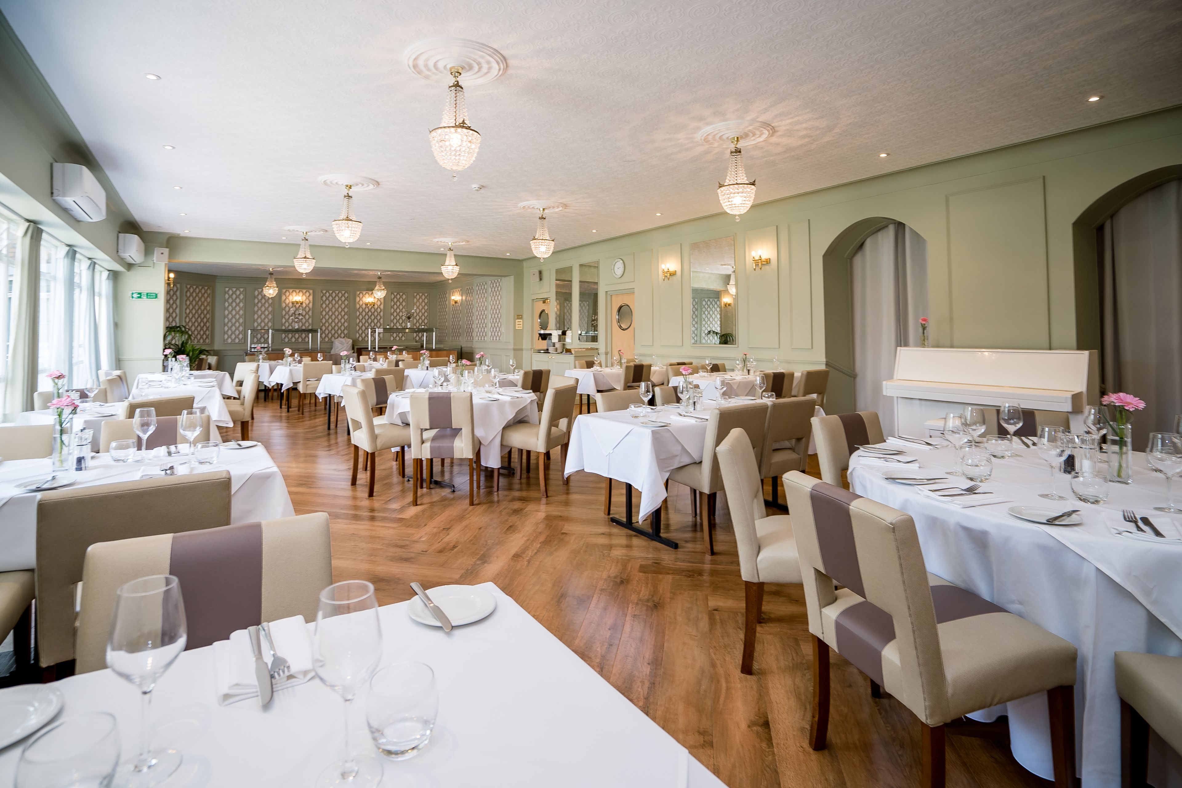 Un comedor amplio con varias mesas dispuestas para comer, candelabros elegantes y un diseño de interiores clásico.