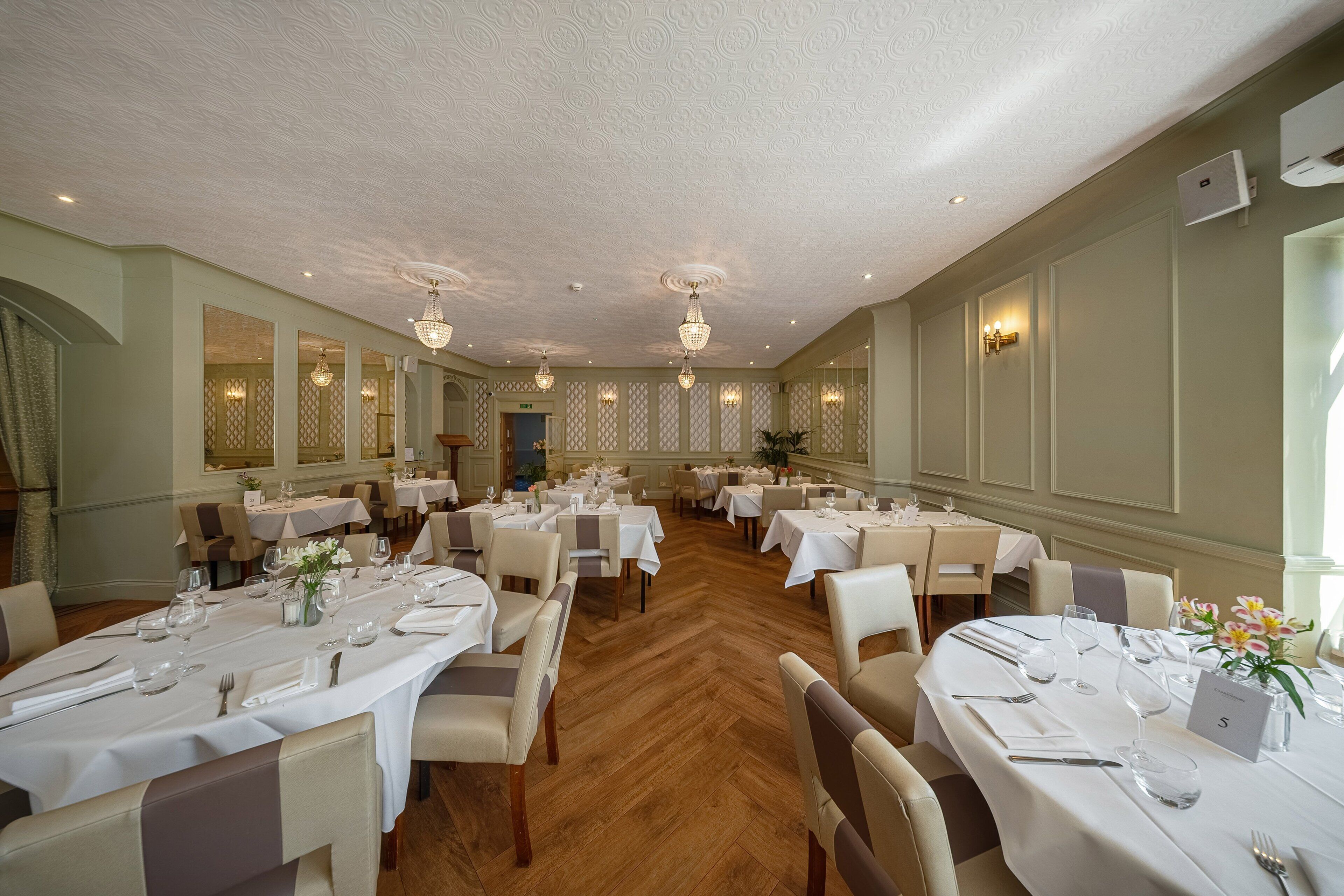 A spacious dining area with multiple tables set for service, elegant chandeliers, and a classic interior design.