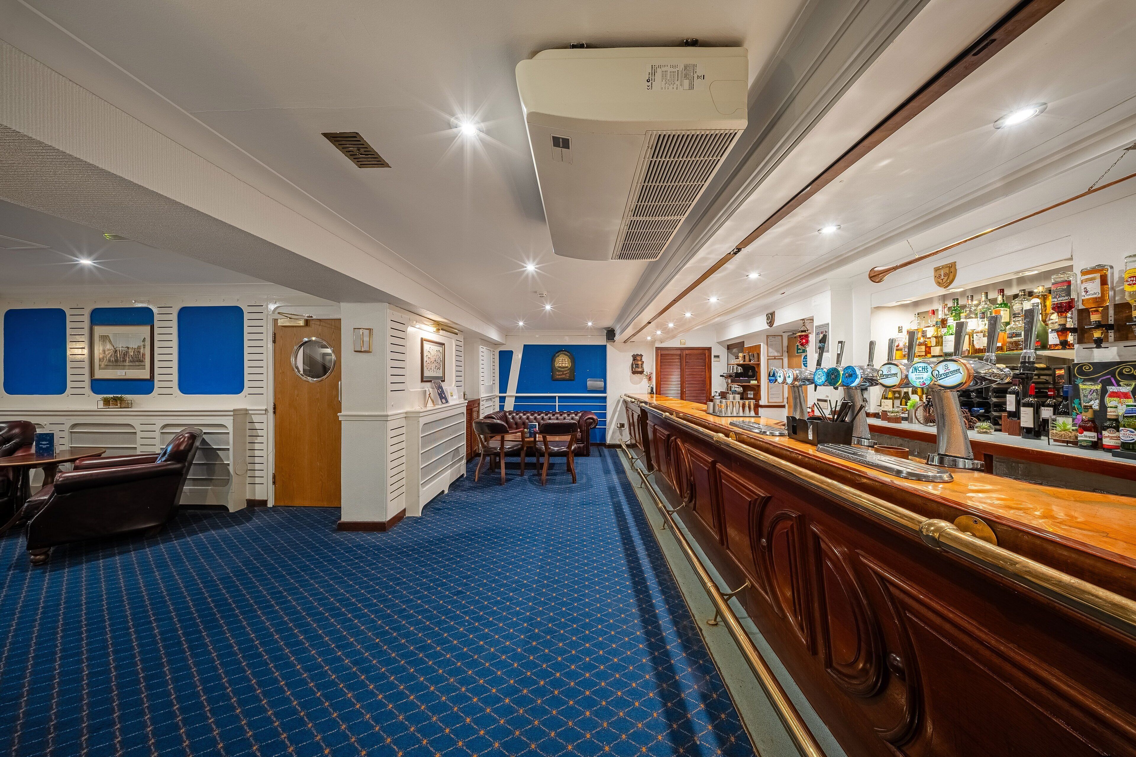 A bar area with a blue patterned carpet, wooden bar counter, and various bottles and glasses.