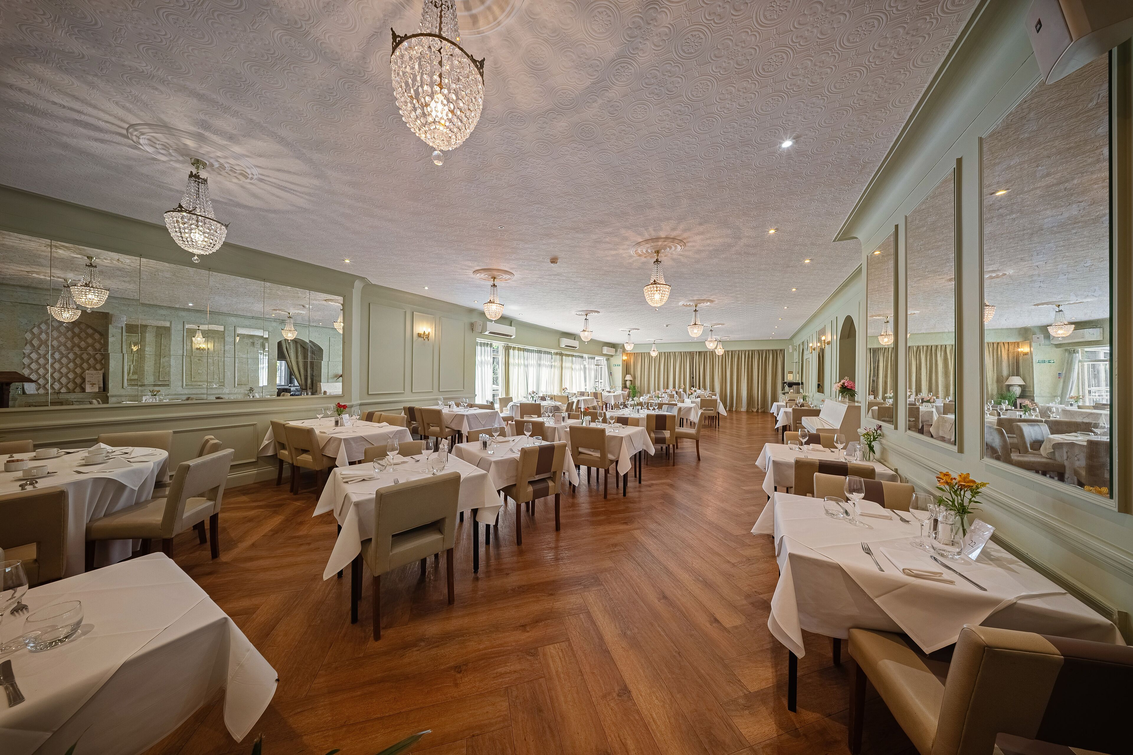 A spacious dining area with multiple tables, chandeliers, and large mirrors.