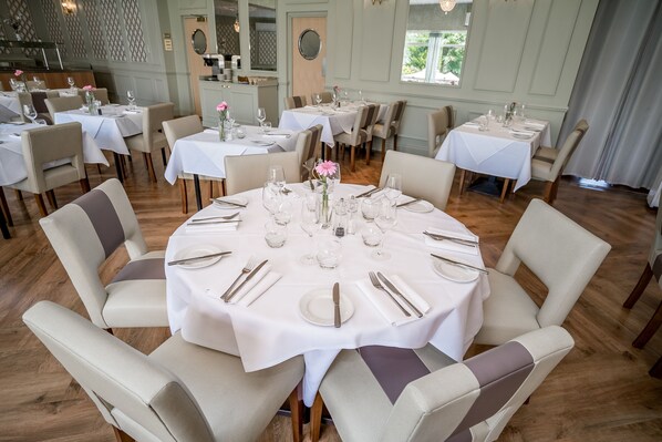 A dining area with round tables set for four, each with white tablecloths, chairs, and fine china.