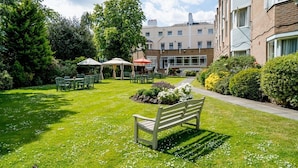 A well-maintained garden with a wooden bench, outdoor seating area, and a building in the background. - The Clarendon Hotel - Blackheath (London)