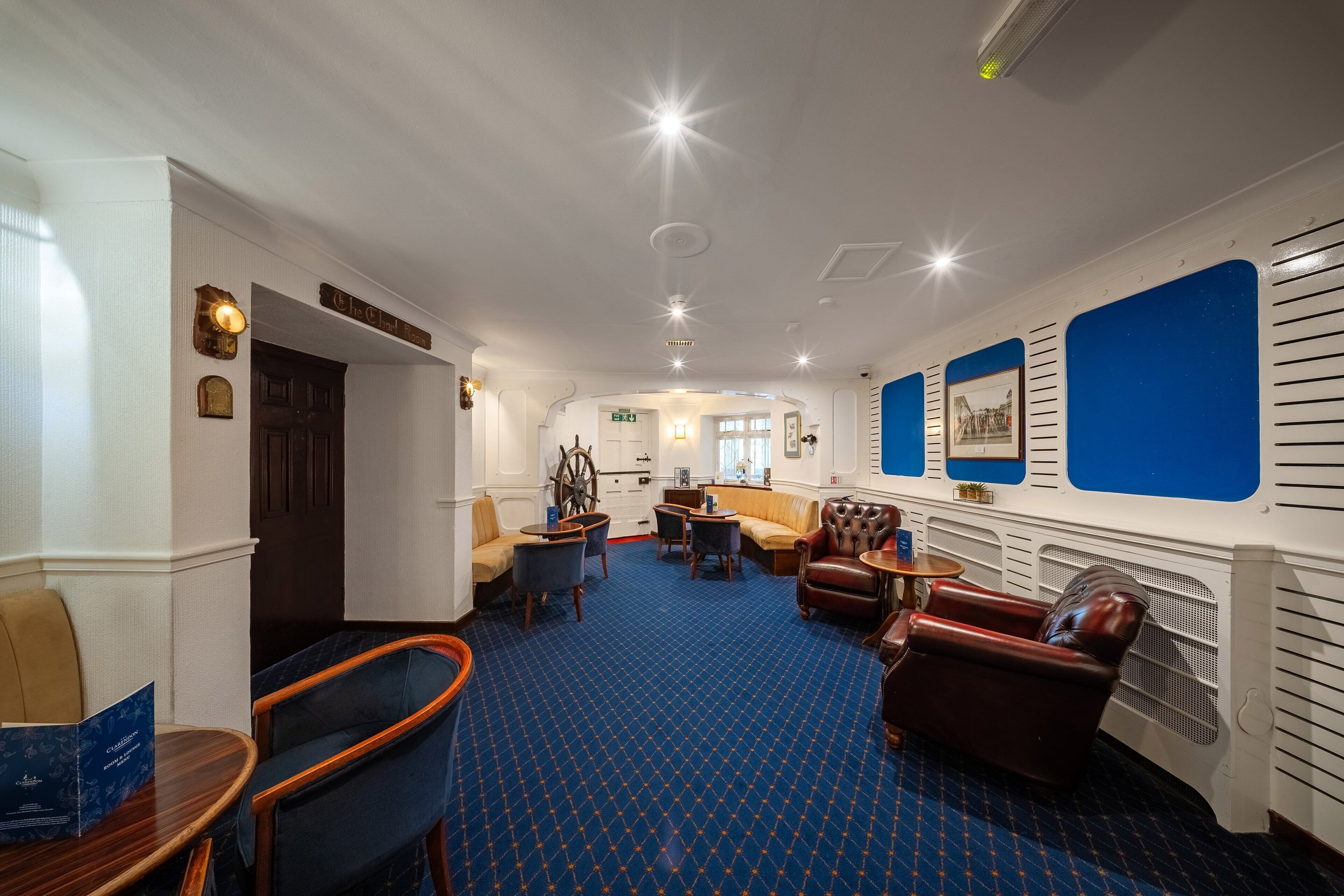 A hotel lobby with a blue patterned carpet, leather seating, and a sign reading "The Club Room."