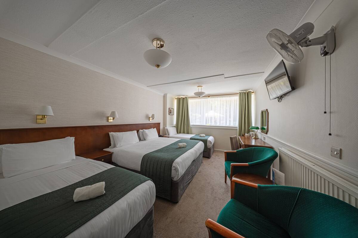 Een hotelkamer met twee bedden, een bureau, een stoel, een televisie en een plafondventilator.