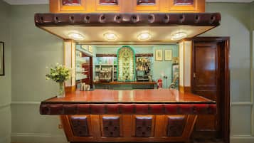 Zona de bar con mostrador de madera, asientos acolchados y un separador de vidrio decorativo.