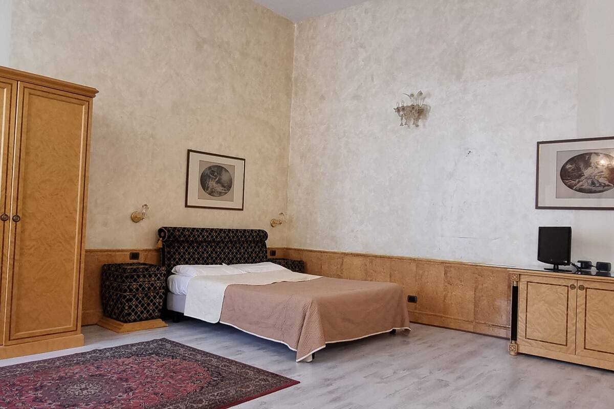 A bedroom with a bed, wooden wardrobe, bedside table, and two framed pictures on the wall.
