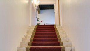 Una escalera con alfombra roja que conduce a una zona de descanso con una planta y una puerta.