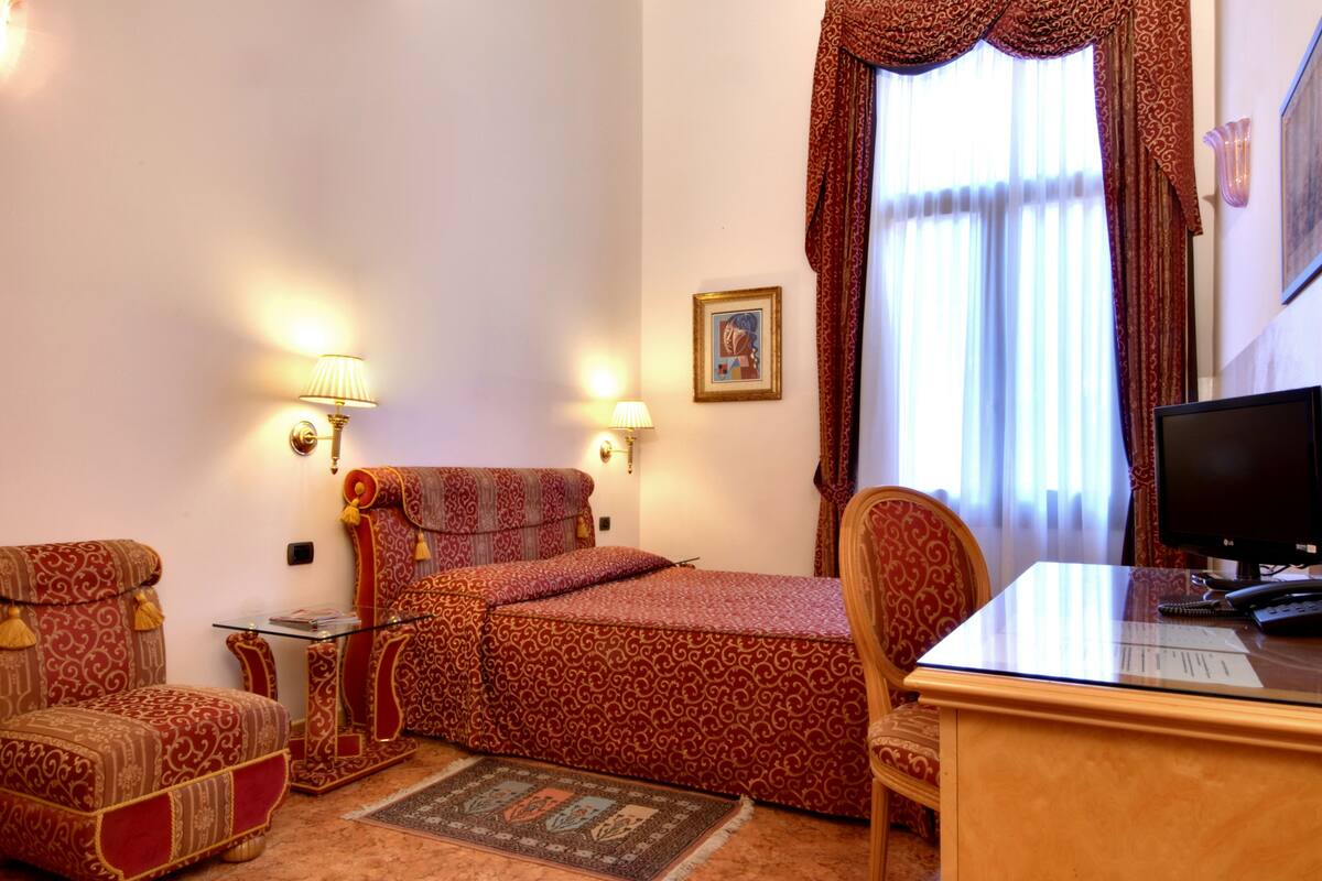 A room with a bed, two armchairs, a desk with a computer, and a window with curtains.