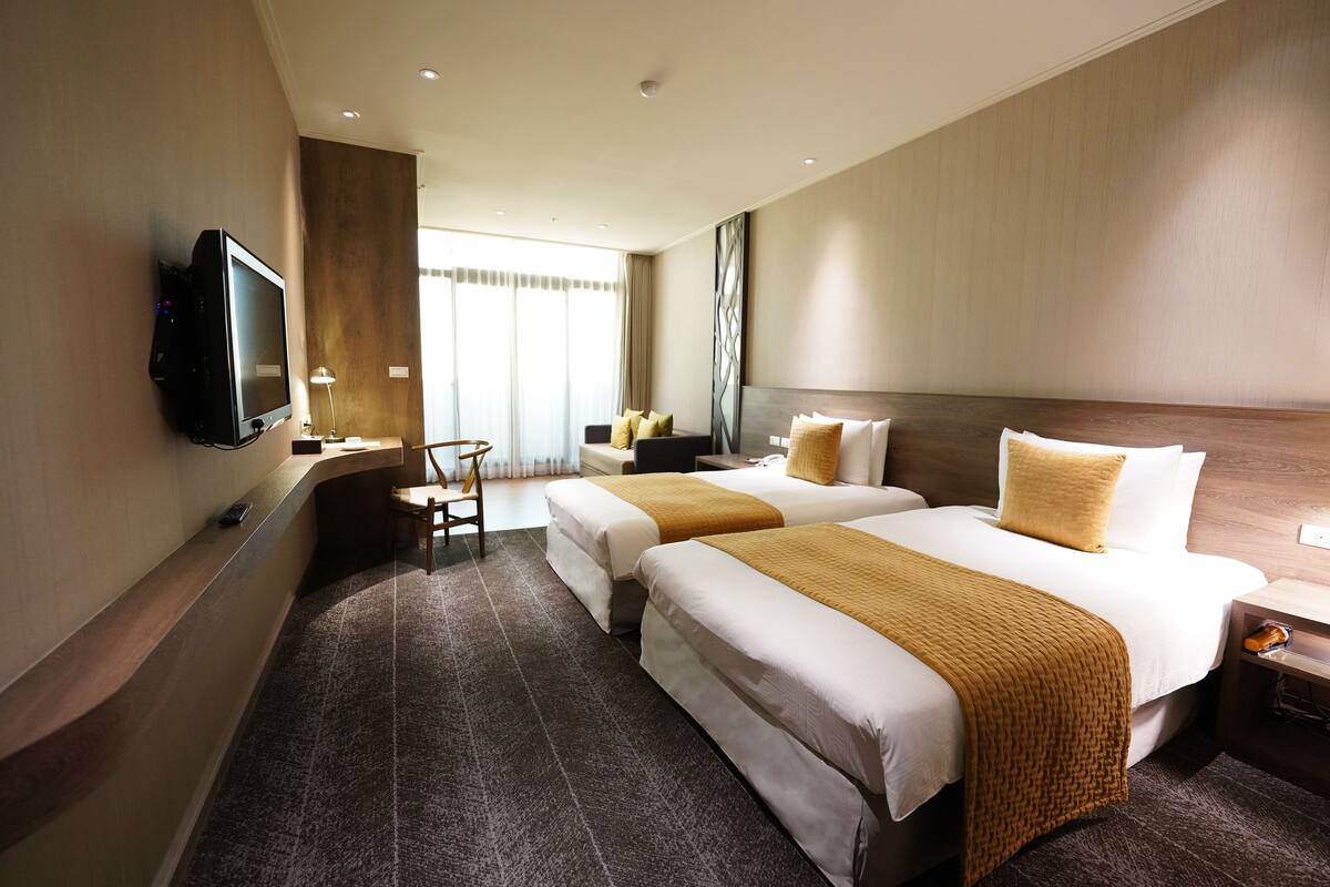 A hotel room with two beds, a TV, a desk, and a chair.