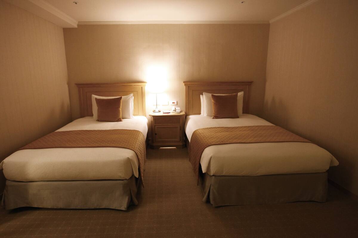 A hotel room with two beds, a nightstand, and a lamp.