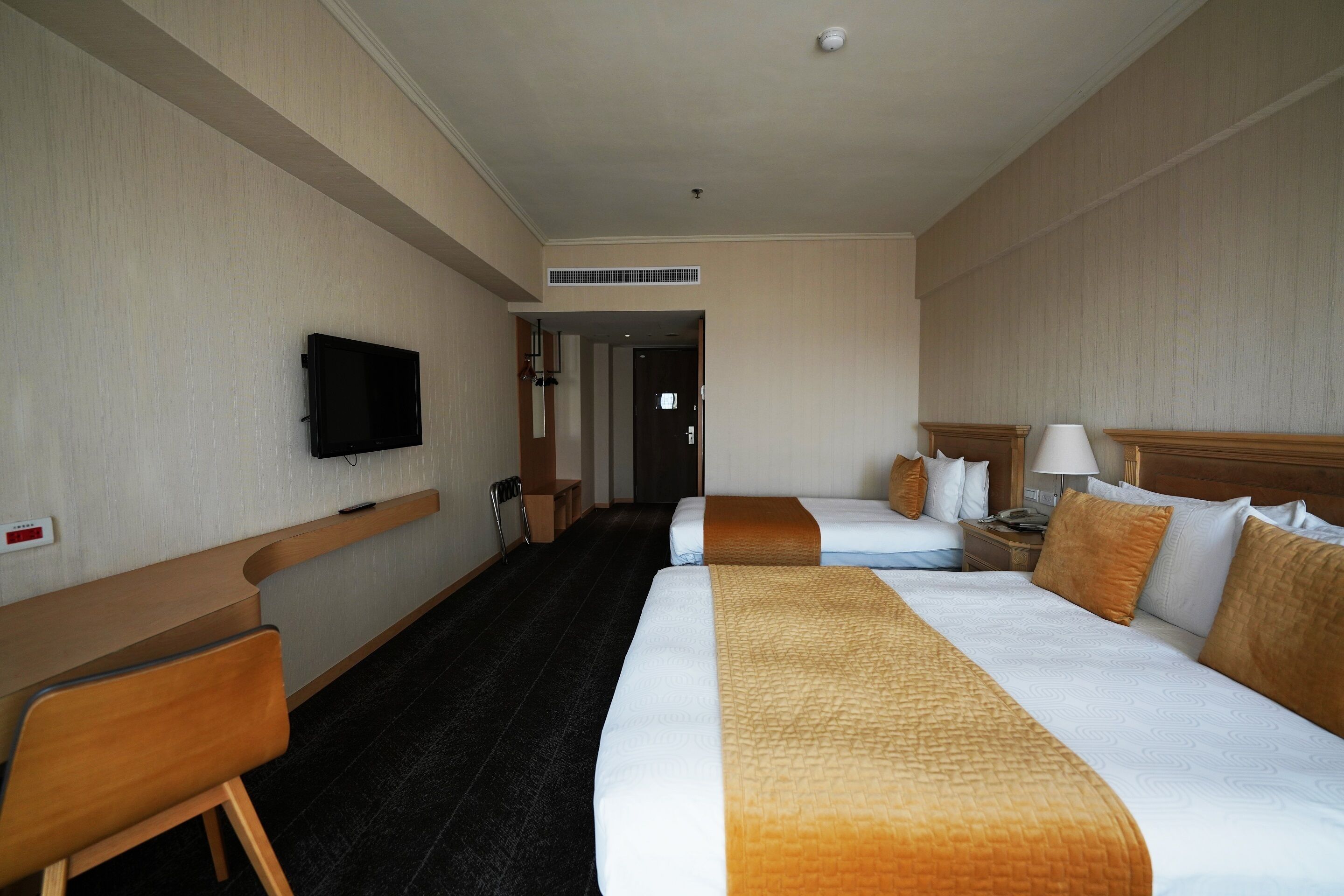 A hotel room with a large bed, a desk, a chair, a TV, and a door leading to another room.