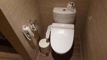 A compact bathroom with a toilet, bidet, and a toilet paper holder.