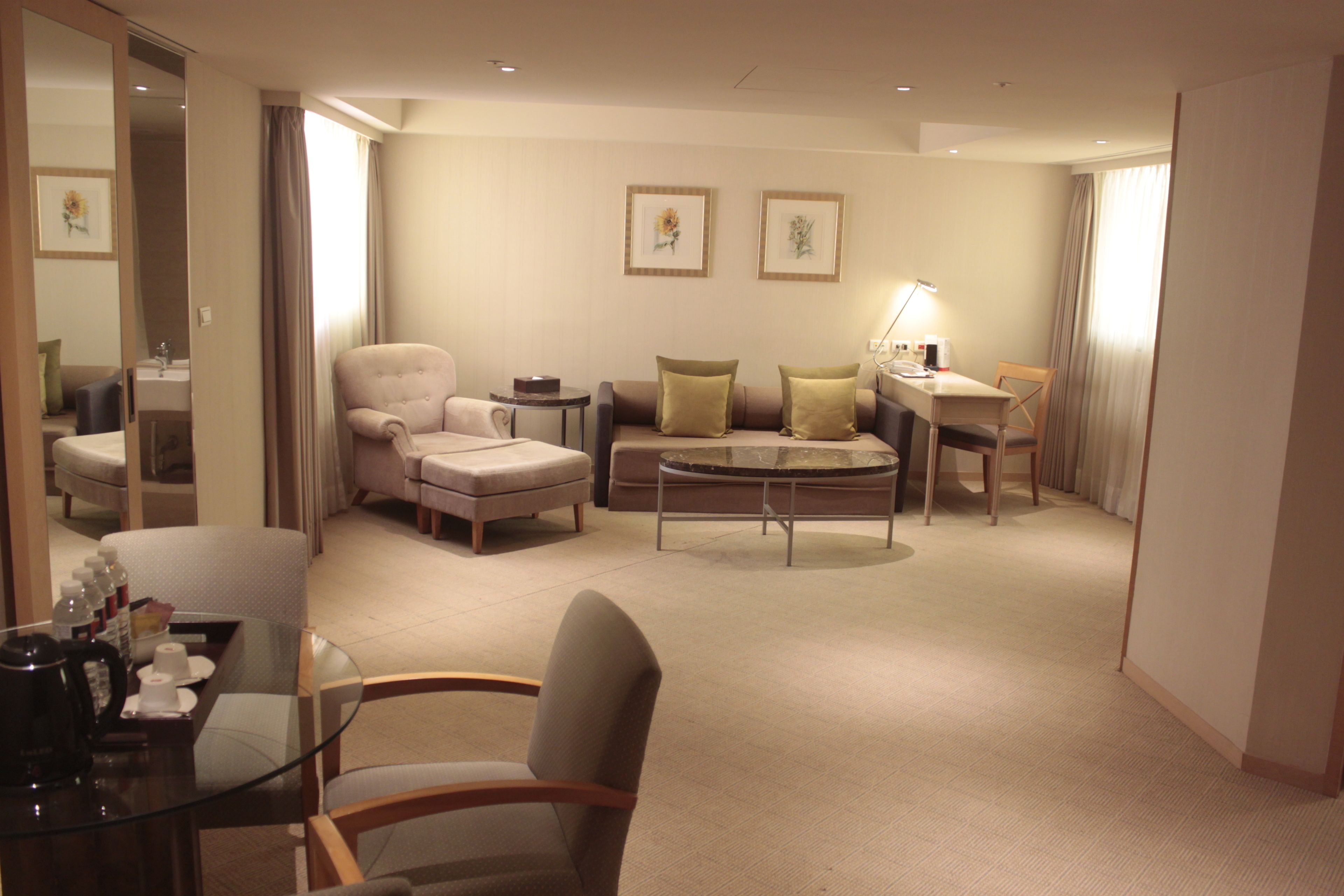 A hotel room with a sitting area featuring a sofa, armchairs, a coffee table, and a small desk with a lamp.