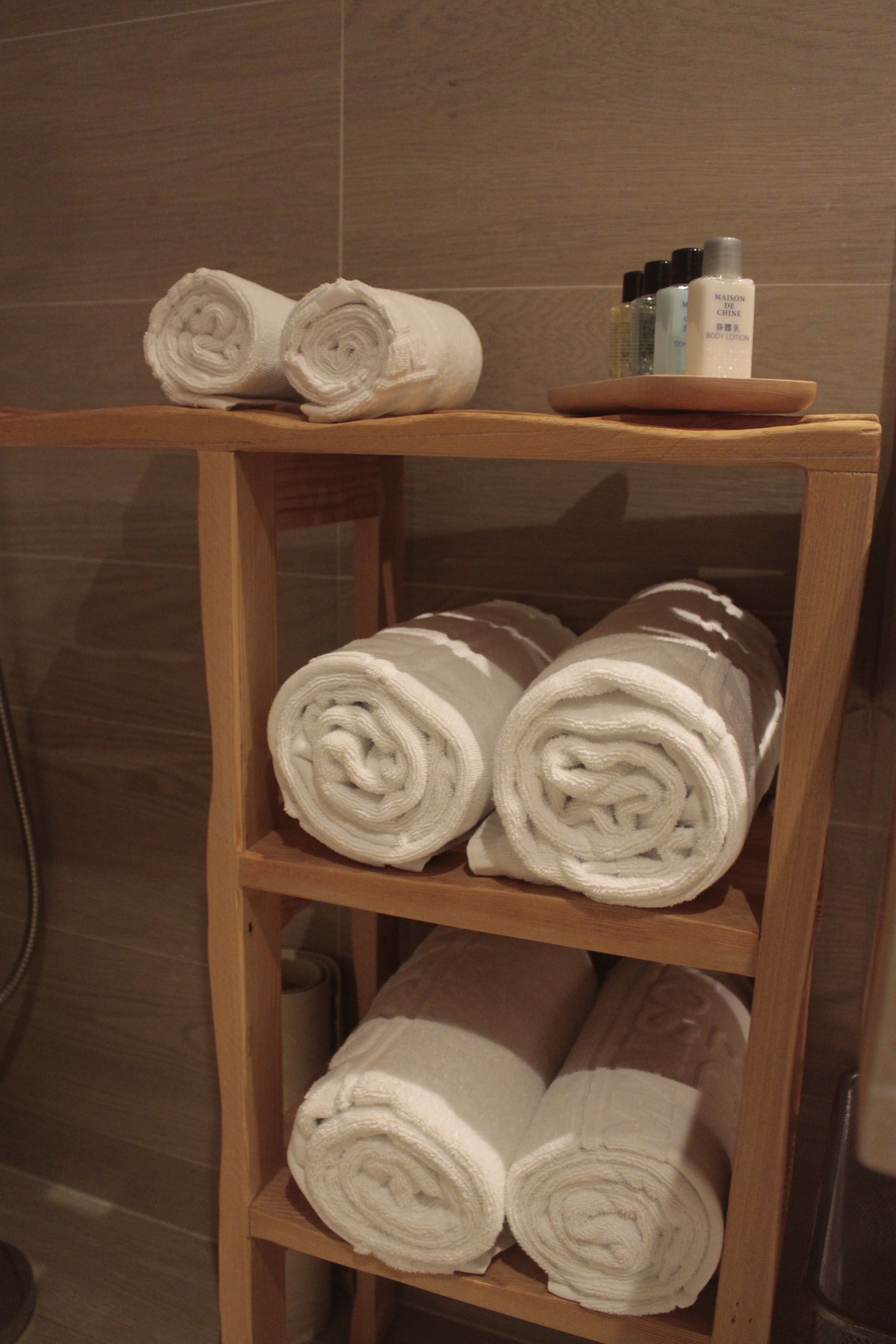 A wooden shelf with neatly rolled white towels and a small tray with toiletries.