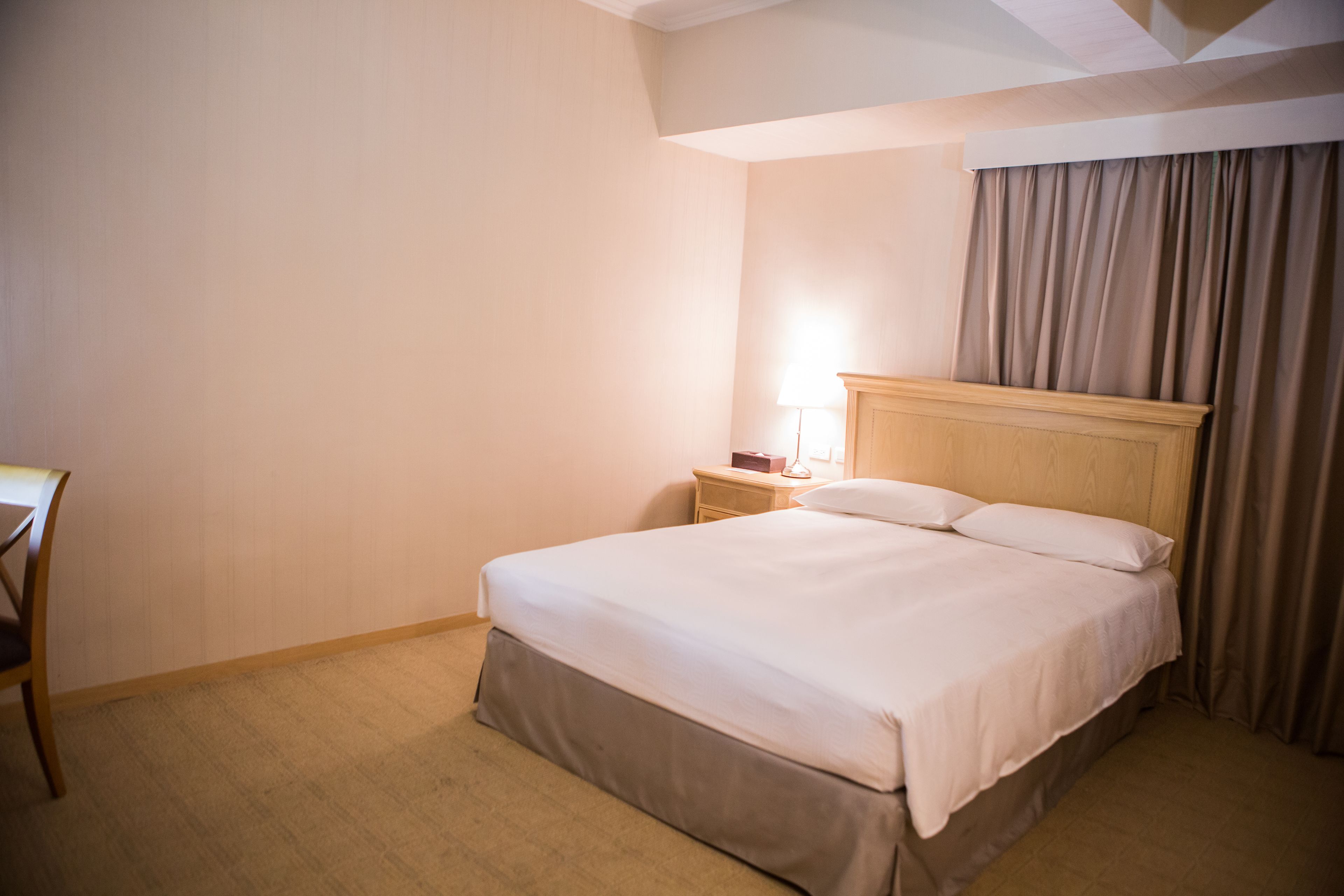 A hotel room with a bed, a nightstand, a lamp, and a chair.