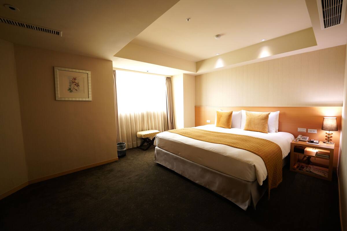 A hotel room with a large bed, bedside table, and a window with curtains.