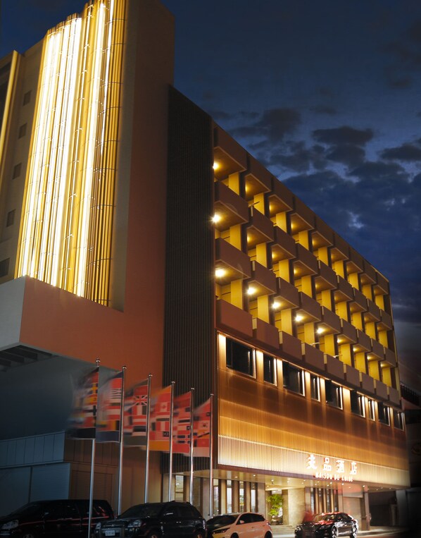 Un hotel moderno con una llamativa estructura de luces verticales, varios balcones y una entrada visible con banderas.
