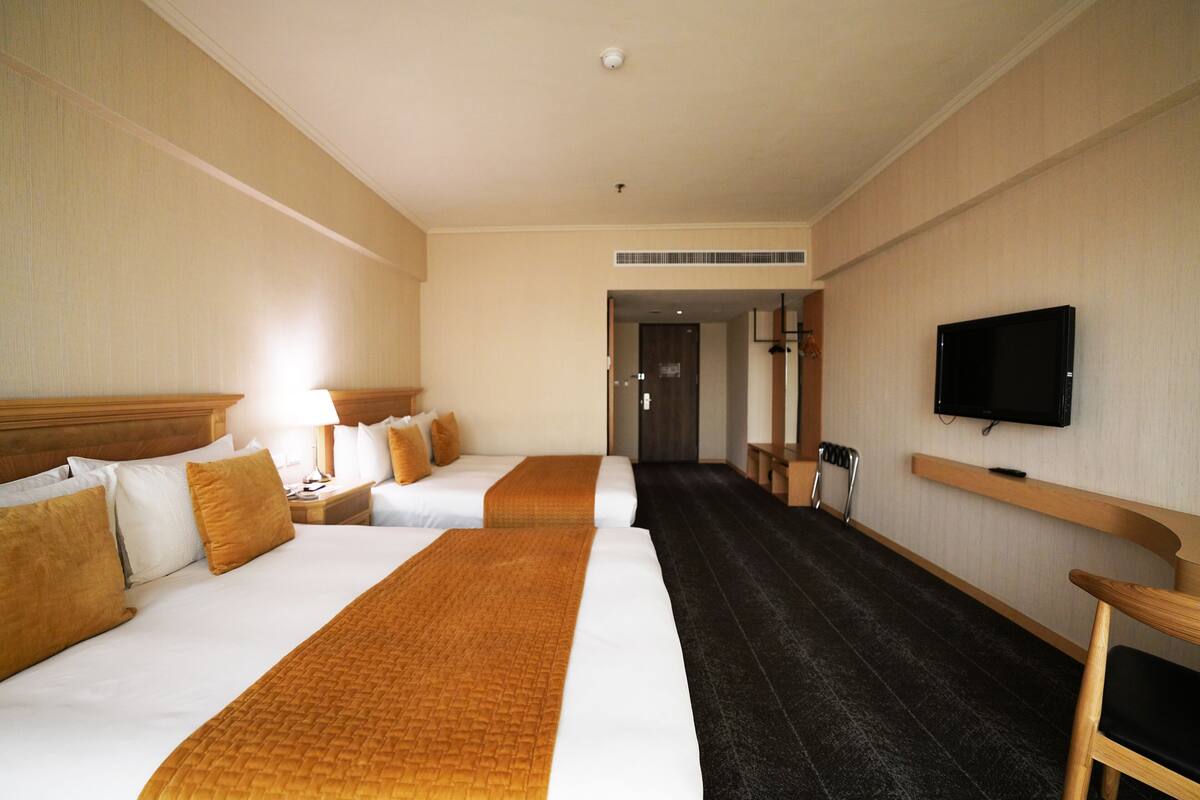 A hotel room with two beds, a television, and a hallway leading to another room.