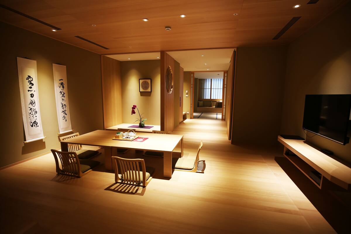 A modern dining area with a wooden table and chairs, a TV on the right, and traditional Japanese calligraphy on the walls.