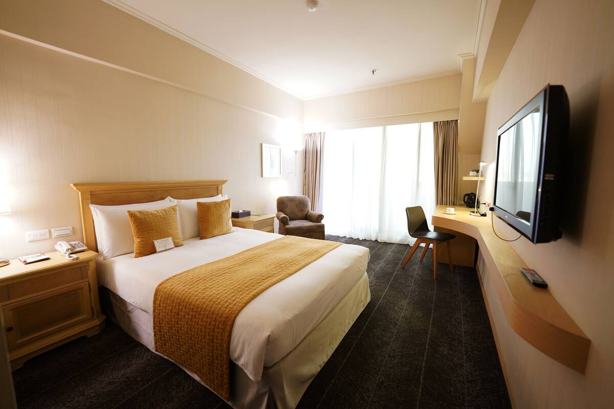 A hotel room with a large bed, a desk, a chair, a television, and a nightstand.